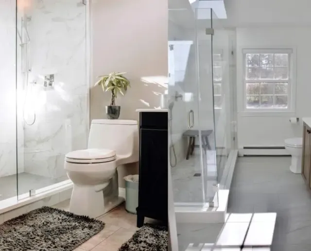 Side-by-side small bathroom designs with clear glass showers, marble-look tile walls and compact vanities by Shapiro Bathrooms & More.