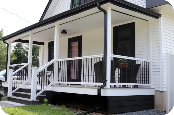 White house with a covered front porch, black railing, and stairs on the left.