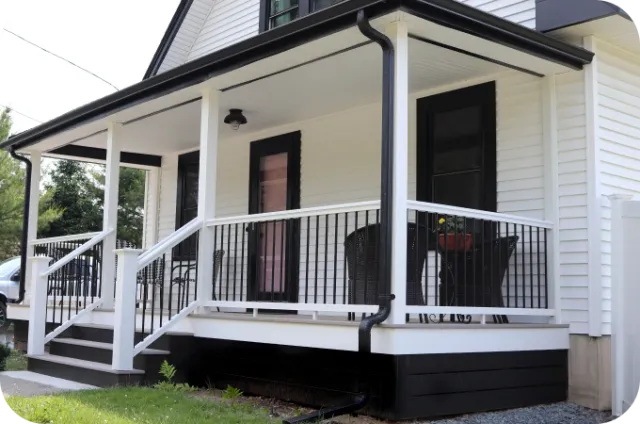 White house with a covered front porch, black railing, and stairs on the left.
