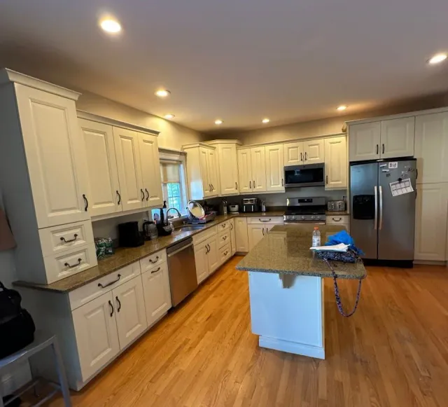 Modern kitchen with white cabinets, stainless steel appliances, island with seating, hardwood floors, and pendant lighting.