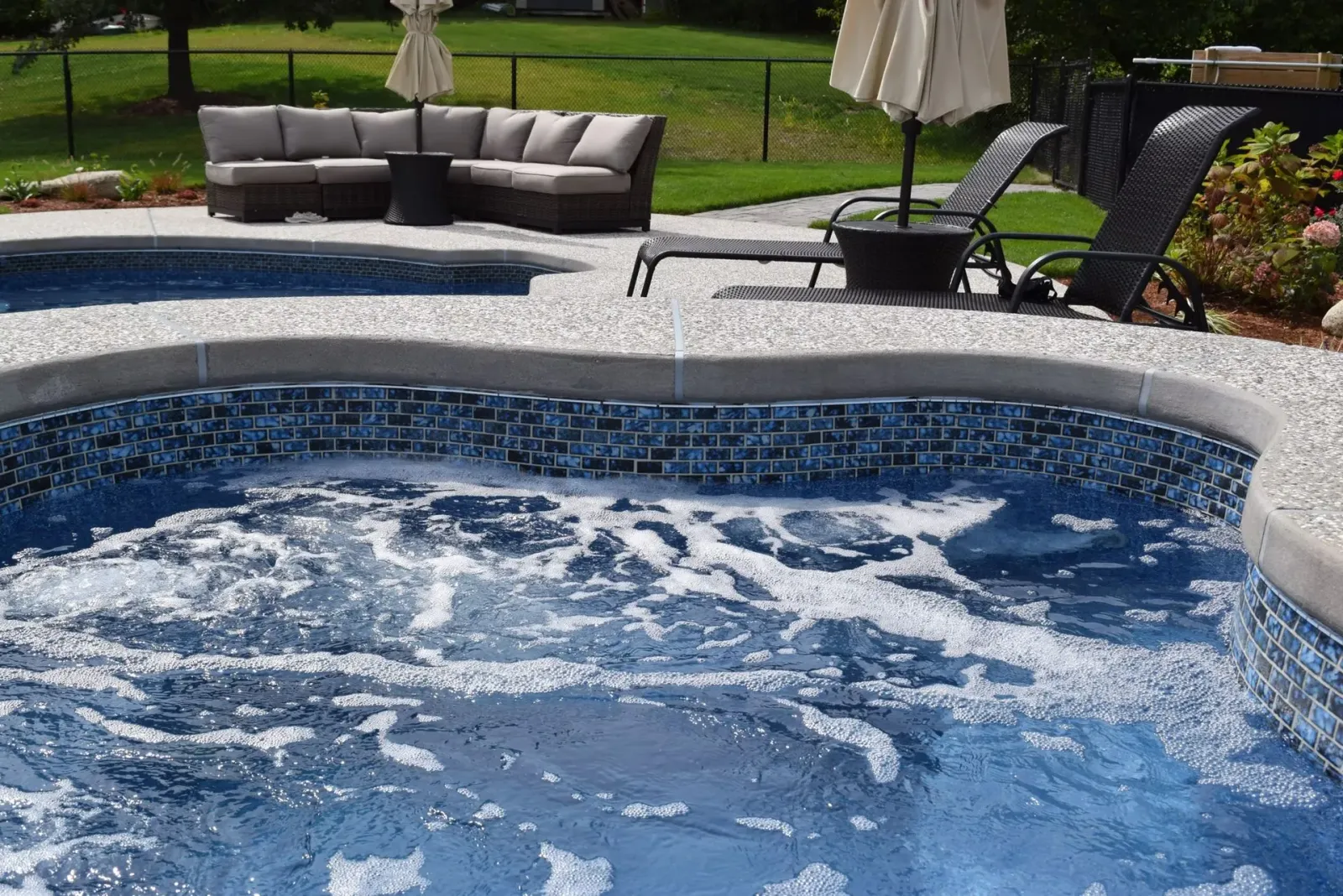 Hot tub with bubbling water, blue tile, and surrounding patio furniture on a sunny day.