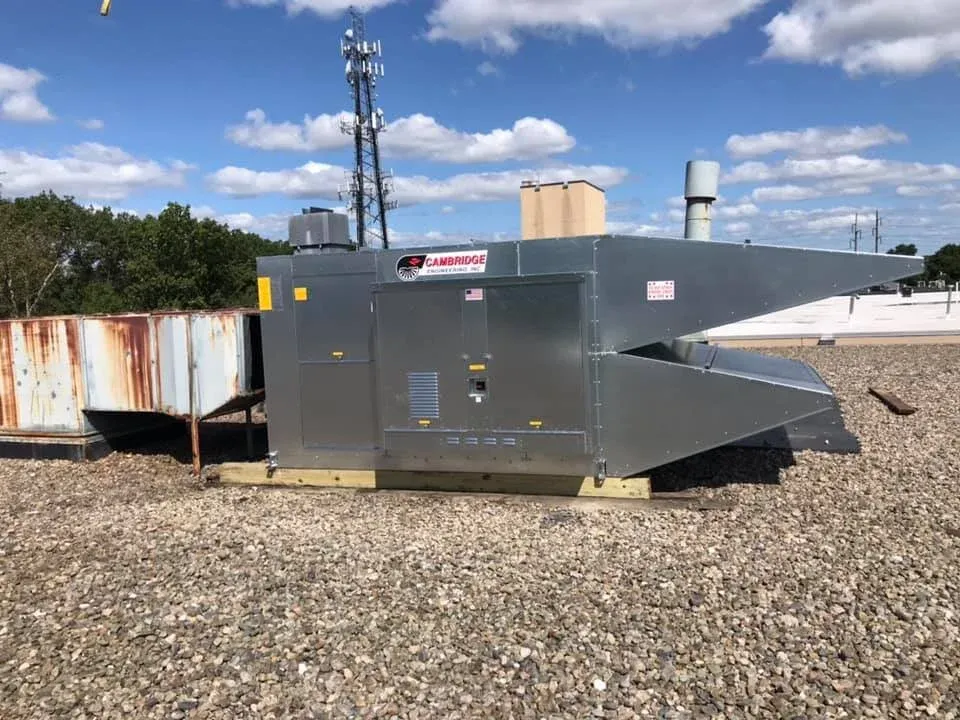 Rooftop industrial HVAC unit on a gravel-covered rooftop with clear blue sky and antenna tower in the background.