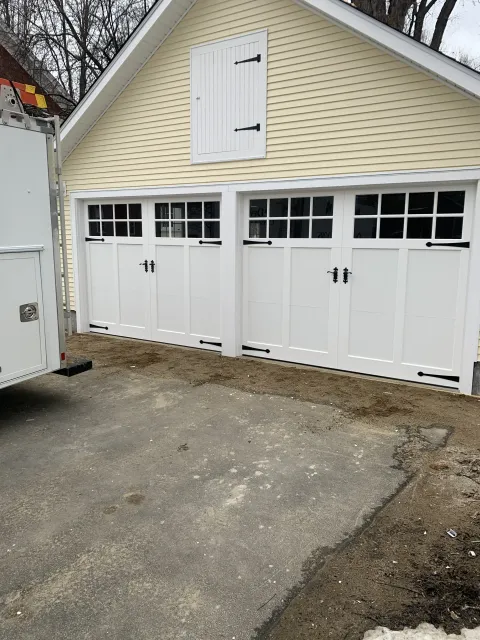 Two white garage doors with black hardware, yellow siding, and an asphalt driveway.