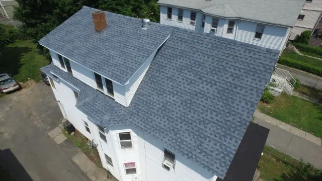 Aerial view of a house with a blue shingled roof and white exterior walls.