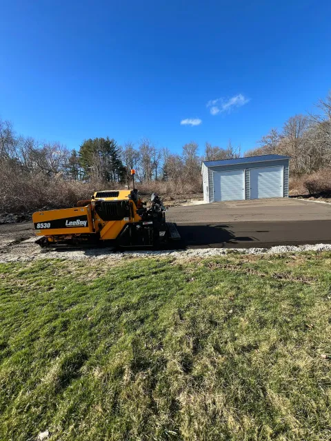 Yellow snowplow clearing snow from a paved driveway on a sunny day.