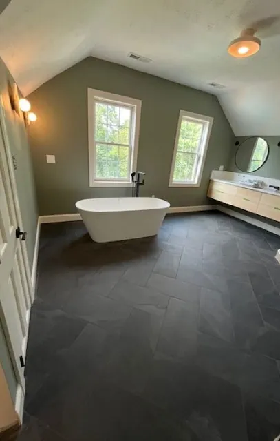 Dreamstate Renovations, LLC - Luxurious bathroom with a freestanding bathtub, modern vanity, and large windows, featuring sleek black tiles and contemporary design elements