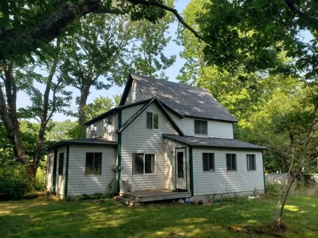A white house with a black roof is surrounded by trees.