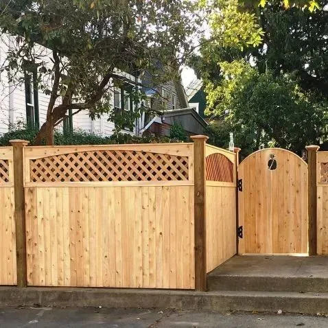 Wooden front fence and gate with lattice detail along a sidewalk, with trees and a house behind it.