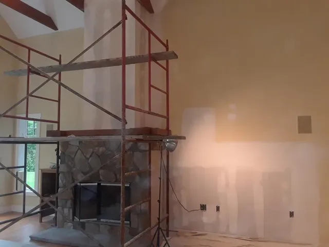 Living room under renovation with red scaffolding beside a stone fireplace and unfinished wall patching