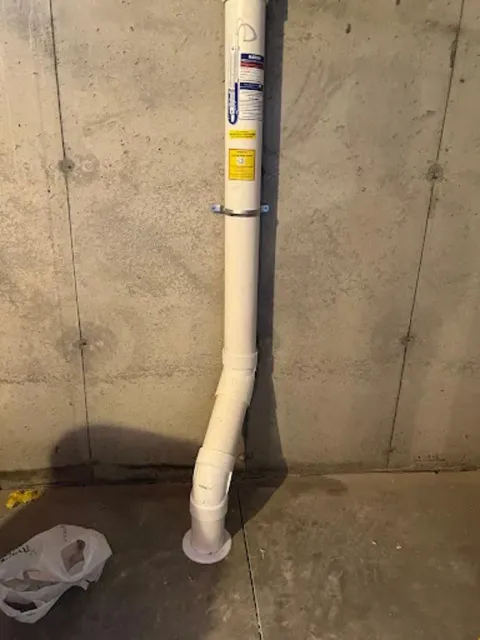 A white pipe is hanging from a concrete wall in a basement.