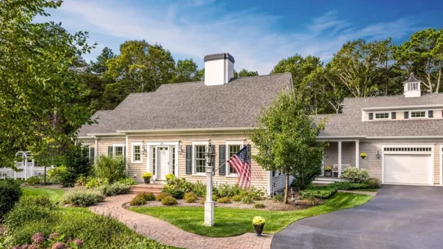 Charming single-story home with gray siding, white trim, brick walkway & flag – McPhee Associates of Cape Cod.