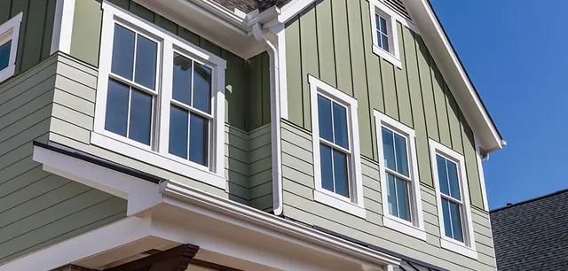 A green house featuring white trim and multiple windows, highlighting its attractive design.