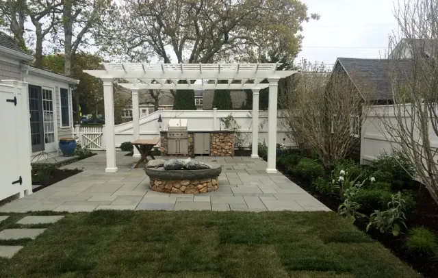 Backyard patio with white pergola, fire pit, stone paving, and landscaped garden beds.