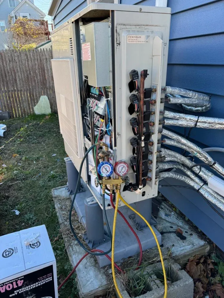 Technician servicing a multi-zone outdoor heat pump unit with refrigerant gauges connected