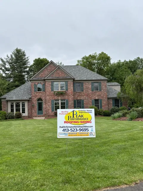 Brick house with a lawn sign advertising a real estate listing under a cloudy sky