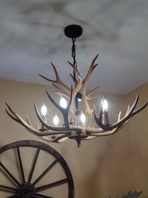 Chandelier made from antlers with five light bulbs, suspended from the ceiling. A wooden wagon wheel is partially visible on the wall behind.