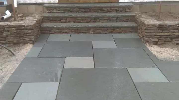 Finished stone patio with steps made of stacked stone in front of a house.