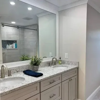 Bathroom vanity with two sinks, a large mirror, a potted plant, a soap dispenser, and a dark blue towel.