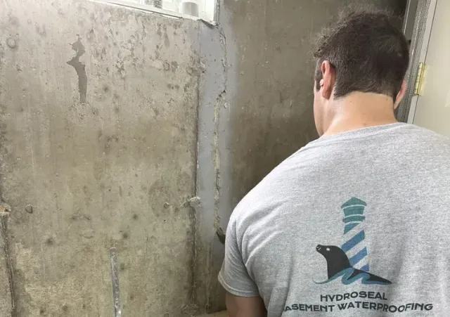 Worker in gray T-shirt applying waterproofing to a concrete wall in a construction setting