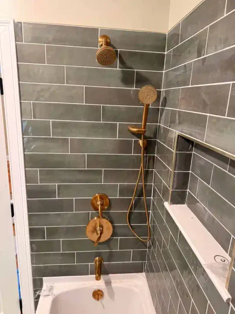 Contemporary shower with bronze showerhead and handheld sprayer in tiled bathroom.