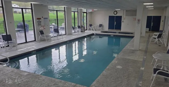 Indoor swimming pool area with chairs along large windows and an outdoor view