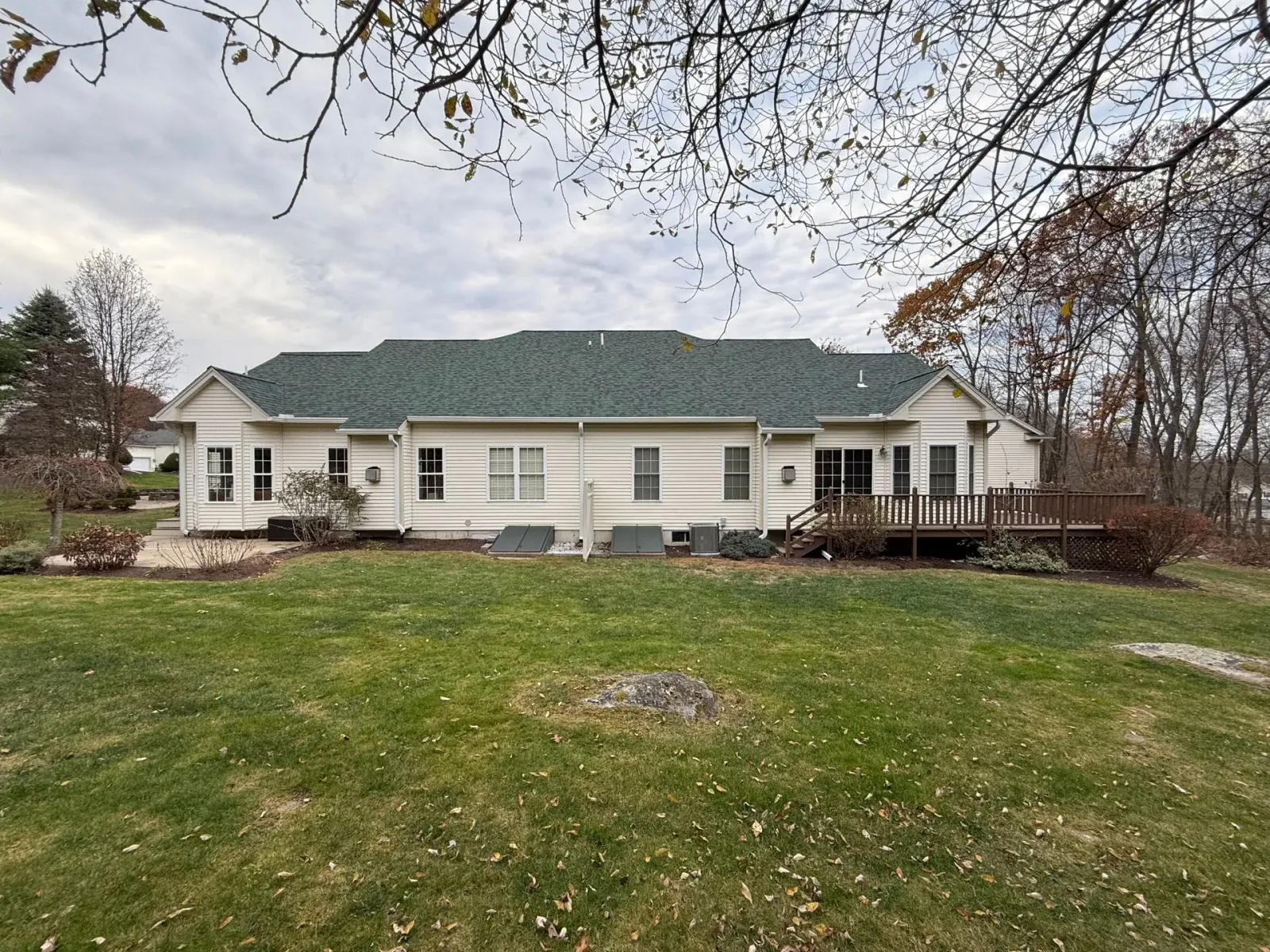 Single-story beige house with a green roof and front porch, set behind a wide grassy lawn