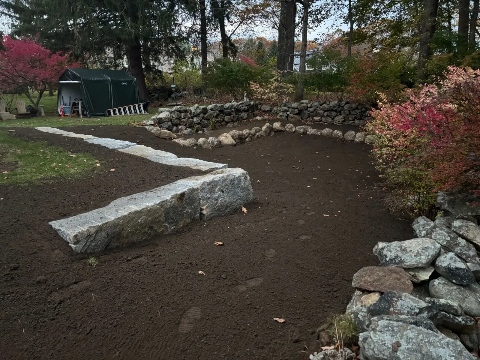 A garden area with dark soil and stone borders, with a path of large stone slabs.