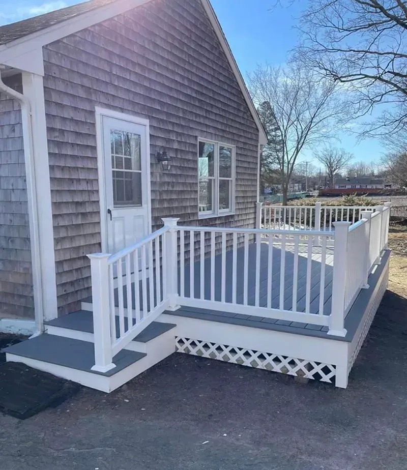 Gray shingled house with white deck and railings; steps lead to the entrance door.