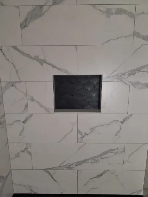 White marble-look tiled wall with a small black square recessed opening in the center.