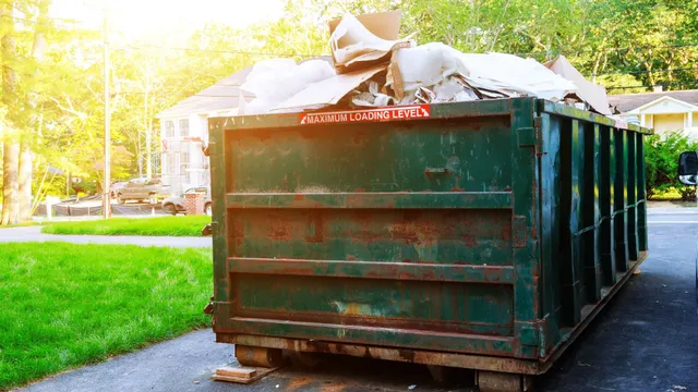 Overflowing green dumpster on residential street with debris and maximum loading sign