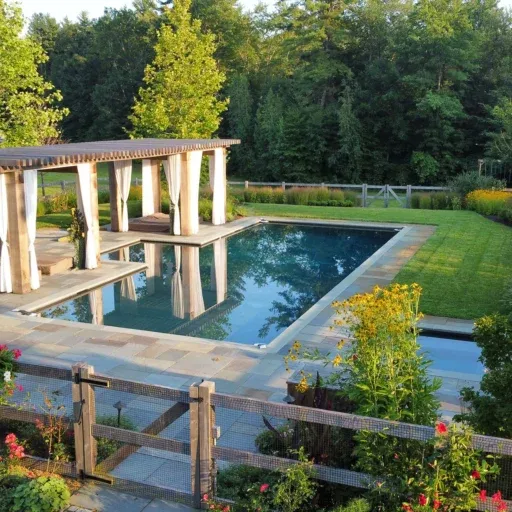 A Carlisle pool landscape blends a cedar pergola, meadow-edge planting, and refined outdoor living design for a relaxed New England backyard retreat.