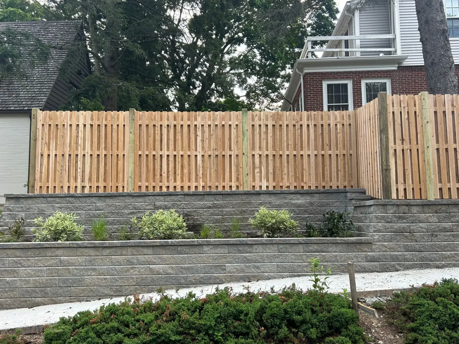 A wooden fence surrounds a stone wall in front of a house.