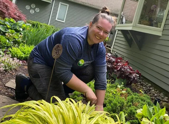 A woman is kneeling down in a garden next to a house.