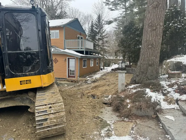 A yellow and black excavator is sitting in front of a house.