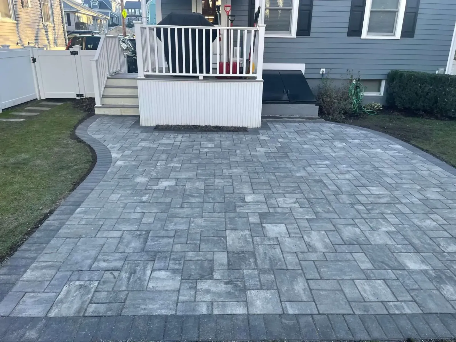 Gray paver patio with a white porch, bordered by green grass.