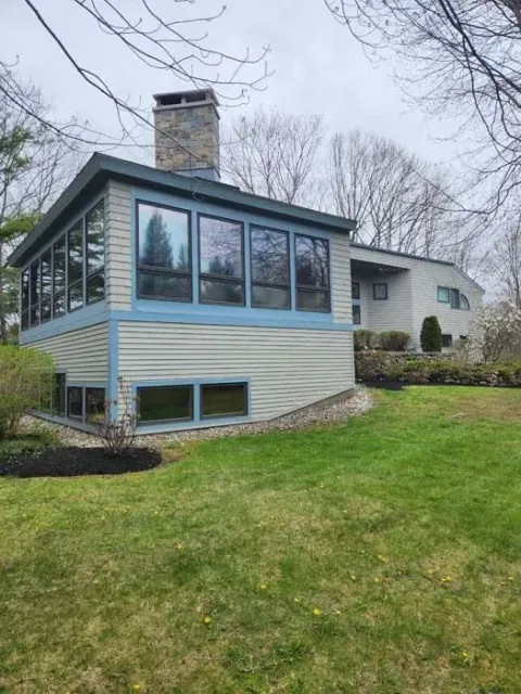 Modern house with large windows, stone chimney, and sloped green lawn in a cloudy setting