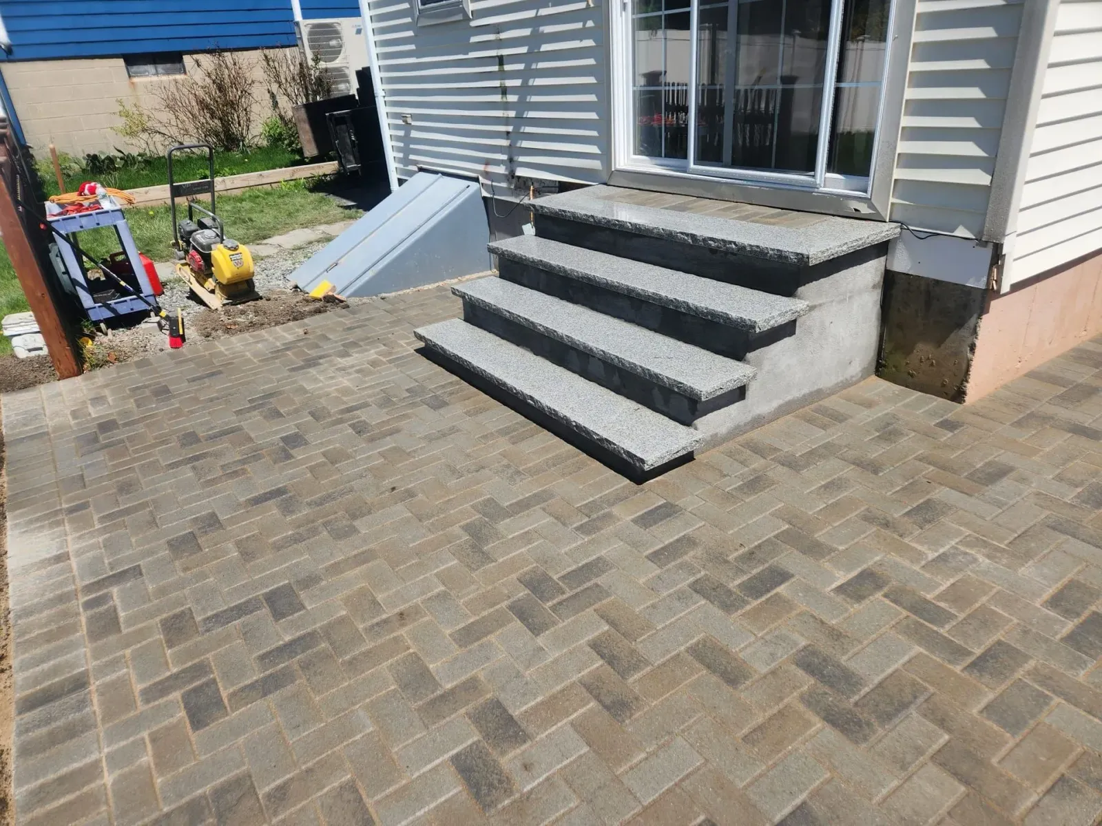 Brick patio with concrete steps leading to a white house entrance, with children’s toys on the left.