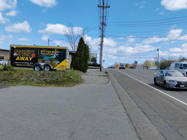 Roadside billboard by a sidewalk beside a parked car and utility poles under a blue sky