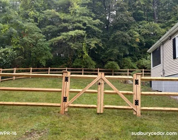 Cedar post and rail dog fence with black wire mesh and matching walk gate installed in a backyard in Sudbury, Massachusetts, providing a secure enclosure while preserving open views.