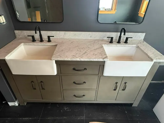 Double-sink vanity with white basins, gray cabinets, marble countertop, and black faucets in a bathroom