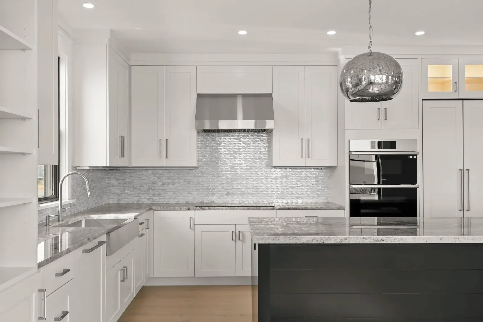 Modern kitchen with white cabinets, marble countertops, a stainless steel range hood, mosaic tile backsplash, and a black island.
