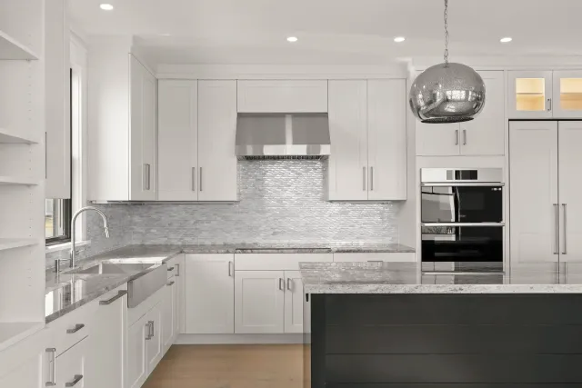 Modern kitchen with white cabinets, marble countertops, a stainless steel range hood, mosaic tile backsplash, and a black island.