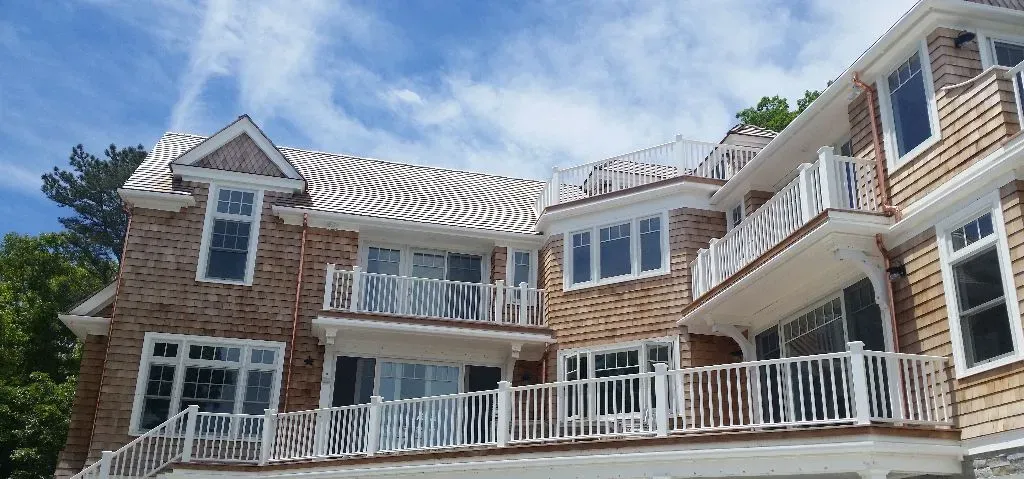 Multi-story house with cedar shake siding, white balconies, and a blue sky background.