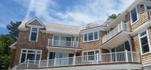 Multi-story house with cedar shake siding, white balconies, and a blue sky background.