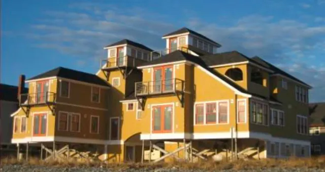 A large, colorful multi-level house with yellow and brown exterior, multiple windows, balconies, and a stairway, set against a blue sky.
