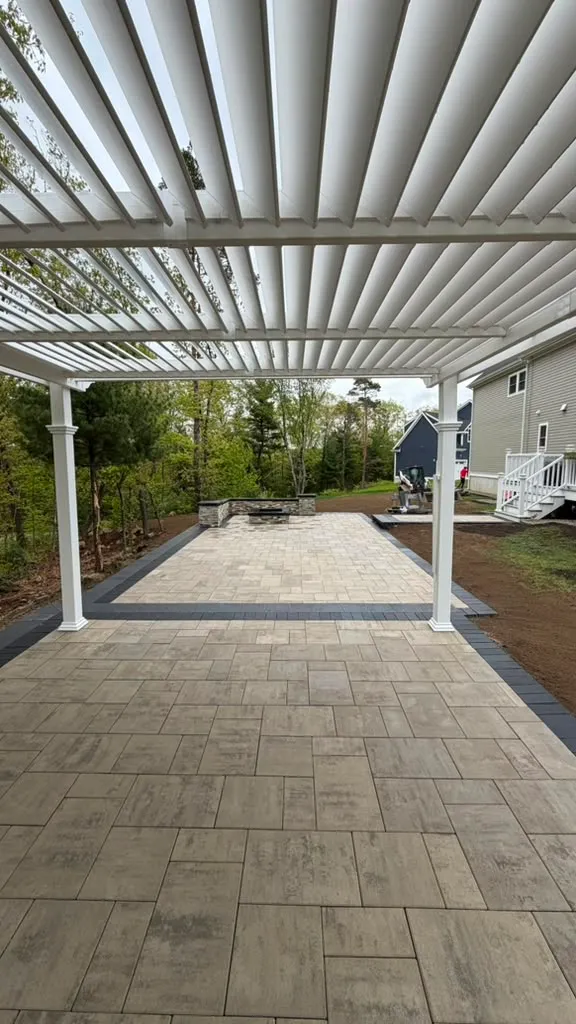 Large paver patio covered by a white pergola with adjustable louvers