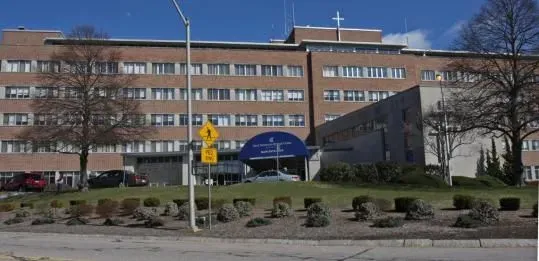 Exterior of a brick building, with multiple stories, likely a hospital with a blue awning over the entrance.