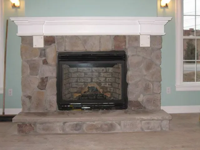A stone fireplace in a living room next to a window