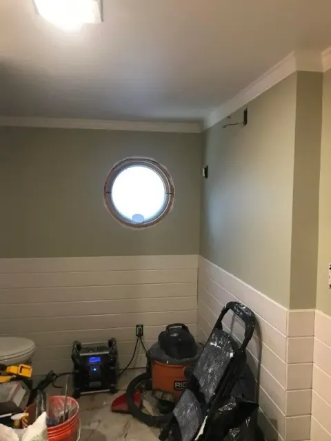 A bathroom with a round window and a vacuum cleaner.