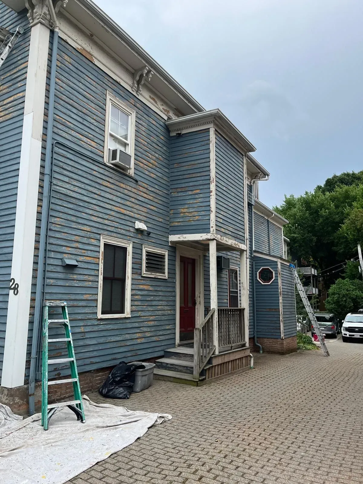 Blue two-story house with white trim, a front porch, ladder, and gravel driveway under construction.